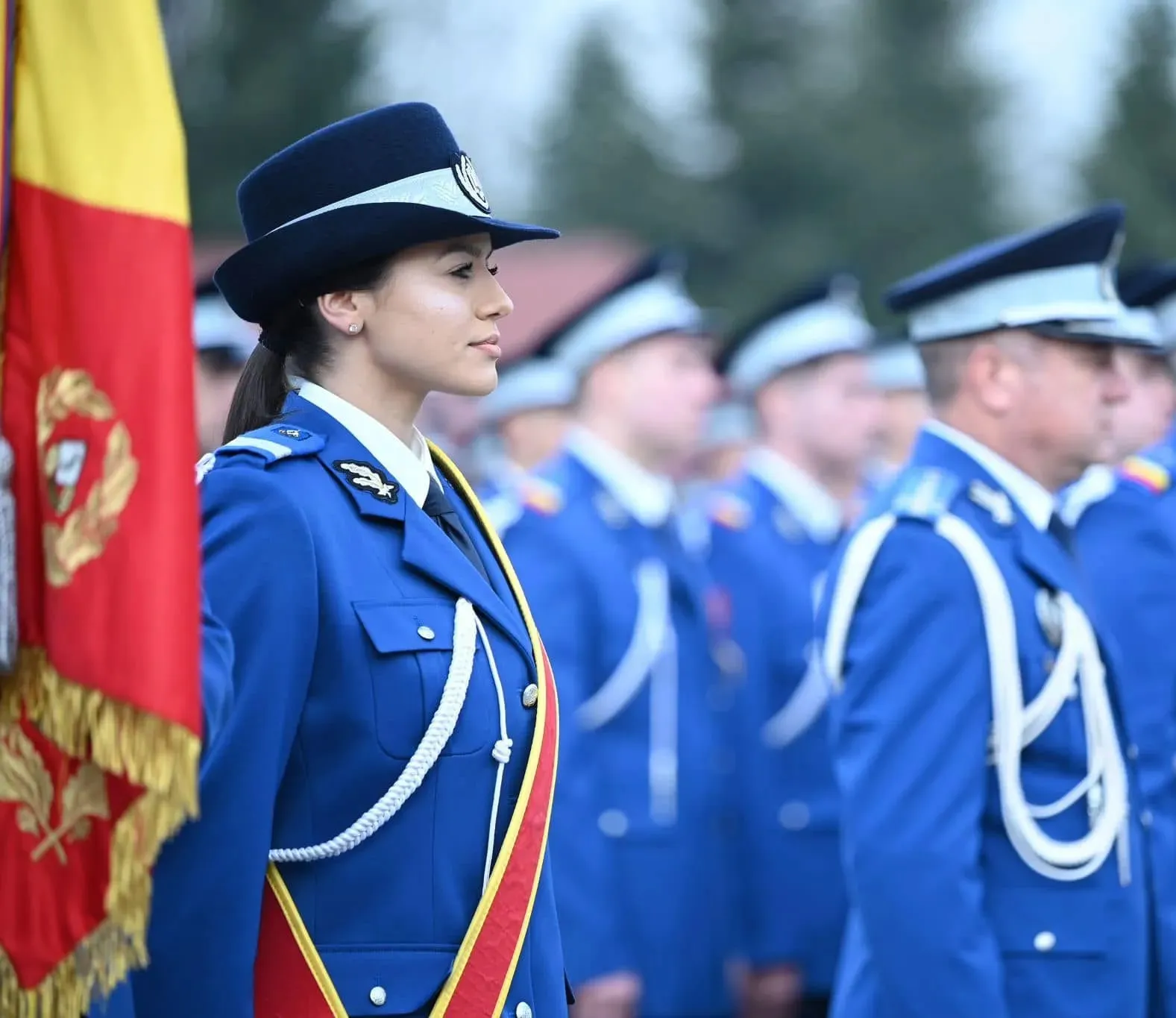 Jandarmeriță în uniformă de ceremonie, lângă drapelul de luptă
