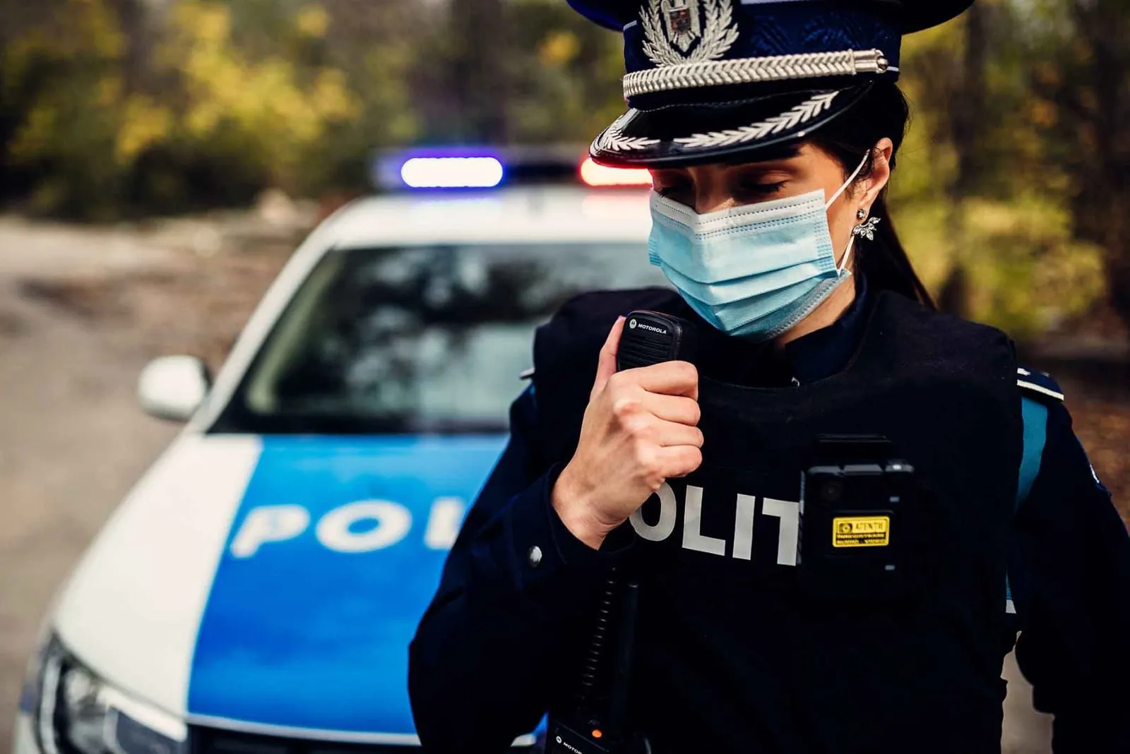 Polițistă în uniformă, transmițând prin stație, lângă autospeciala de poliție